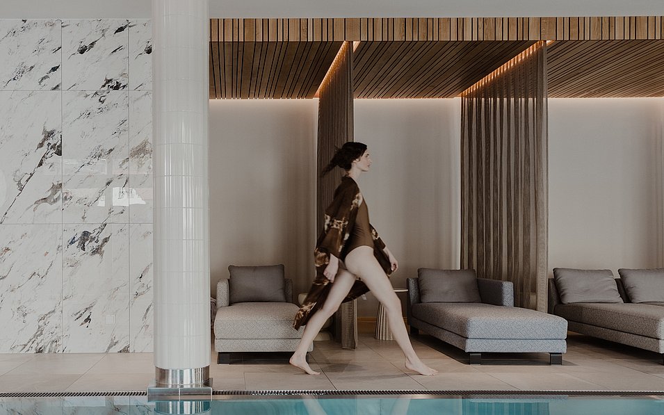 Ein Frau geht durch den Spa Bereich mit Pool und Ruheliegen im Hotel Grand Elisabeth in Bad Ischl im Salzkammergut.