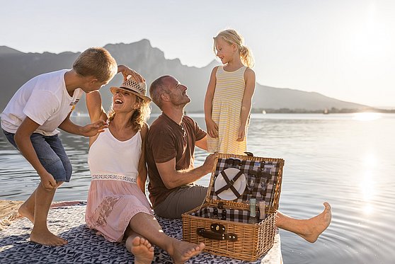 Foto Oberösterreich Tourismus/MondseeIrrsee/Michael Grössinger: Familie auf einem Holzsteg am Mondsee im Salzkammergut beim Picknicken.