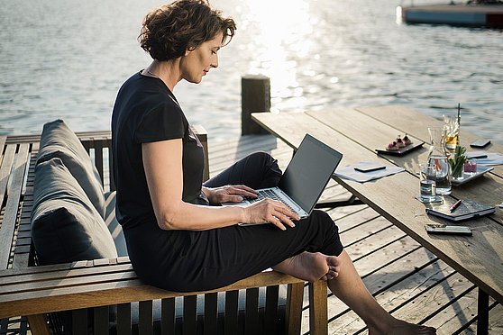 Foto Oberösterreich Tourismus GmbH/Robert Maybach: Eine Frau arbeitet mit ihrem Notebook auf einer Terrasse am See
