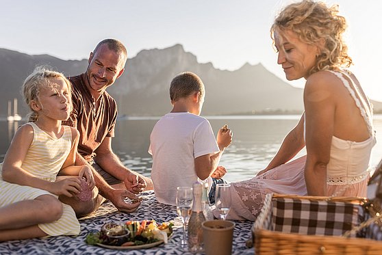 Foto Oberösterreich Tourismus/MondseeIrrsee/Michael Grössinger: Eine Familie mit zwei Kindern beim Picknicken am Mondsee im Salzkammergut.