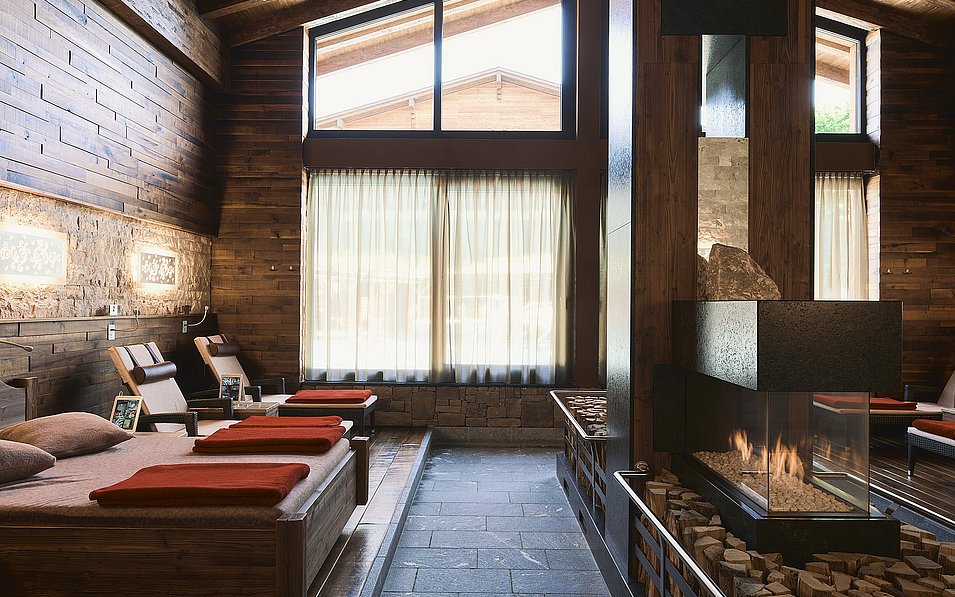 AusZeit - das Sauna-Bergdorf. Innenansicht eines Relaxraumes. In der Mitte des Raumes brennt Feuer im Kamin.