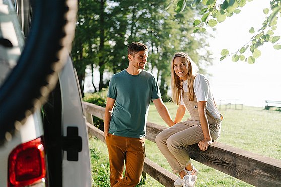 Foto Oberösterreich Tourismus GmbH/Moritz Ablinger: Paar beim Campingurlaub in Oberösterreich bei einem Holzzaun am Straßenrand.
